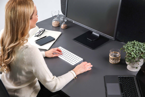 Frau arbeitet im Sitzen an einem höhenverstellbaren Schreibtisch in Schwarz