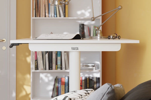 Weißer höhenverstellbarer Schreibtisch im Seitenprofil in einer Wohnung vor einem Bücherregal