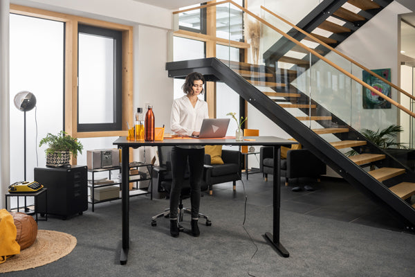 Frau arbeitet im Stehen an einem elektrisch höhenverstellbaren Schreibtisch 160 x 80 cm