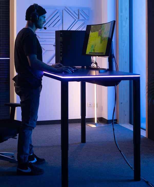 Mann spielt am Computer am höhenverstellbaren Tisch Desk Four mit LED-Beleuchtung.