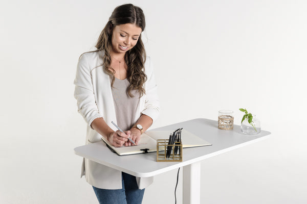 Frau arbeitet im Stehen an einem höhenverstellbaren Schreibtisch in weiß