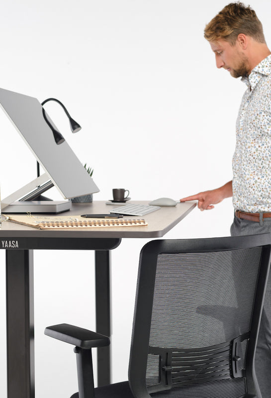 Mann verstellt die Höhe des höhenverstellbaren Tisches Desk Pro 2 in der Farbe Eiche.
