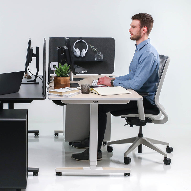 Mann arbeitet sitzend am Yaasa Desk Pro 2 in der Farbe Akazie.